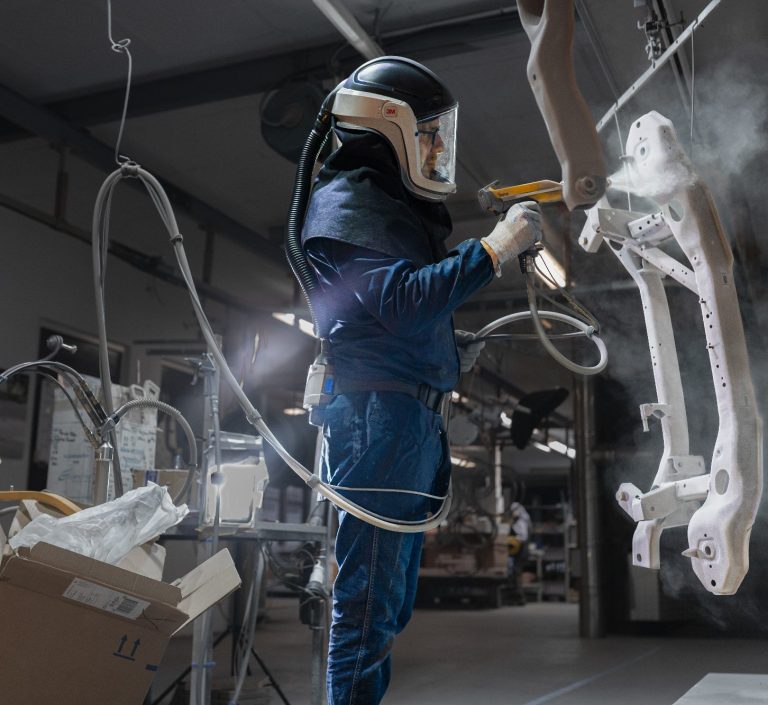 Foto eines Arbeiters in Schutzkleidung der Farbe auf einen Rahmen in einer Werkstatt sprüht.