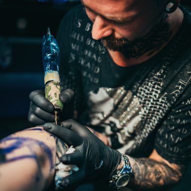 Ein Tätowierer arbeitet an einem Tattoo auf dem Oberschenkel eines Kunden.
